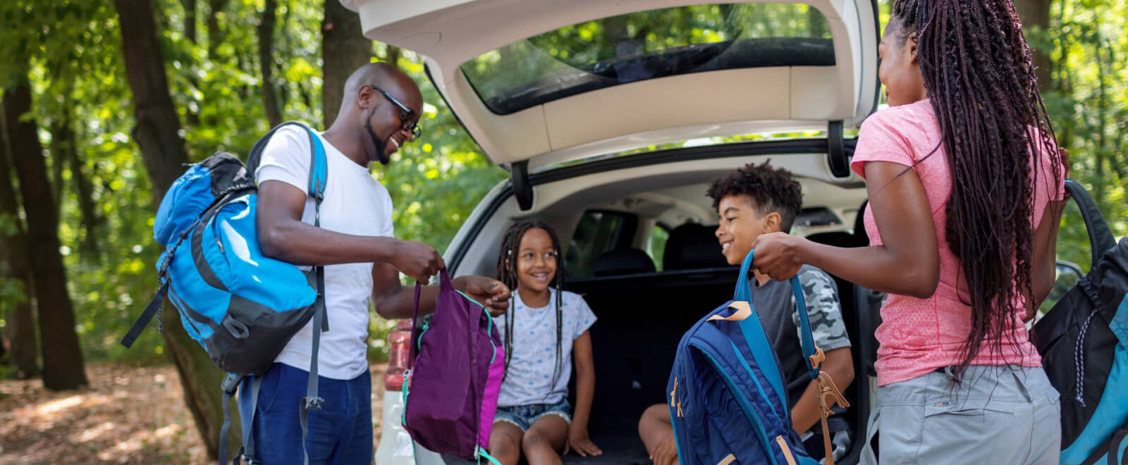 Young family taking backpacks out of the back of an SUV